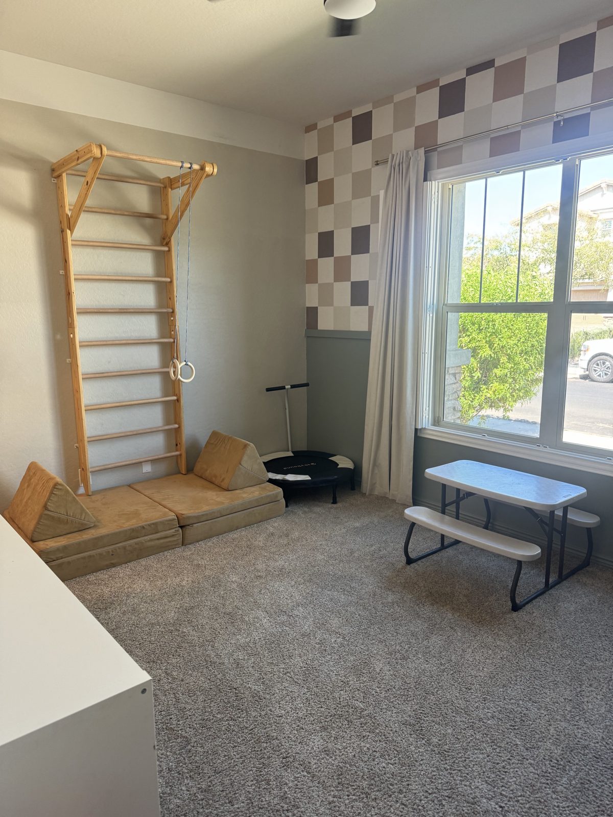 Playroom with a hand-painted tan and brown checkered accent wall, wooden climbing wall and window